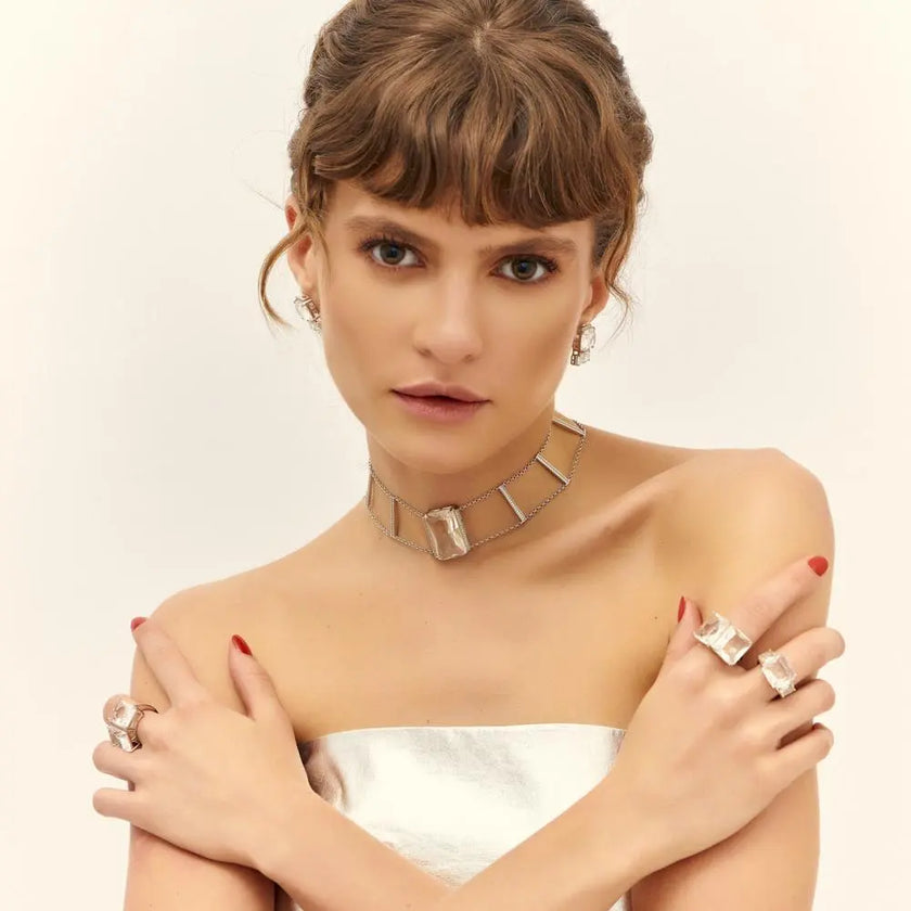 Choker ICE Cristal em ródio branco combinada com anéis e brincos da coleção ICE, evidenciando o brilho do cristal retangular transparente e o design arquitetônico da peça.